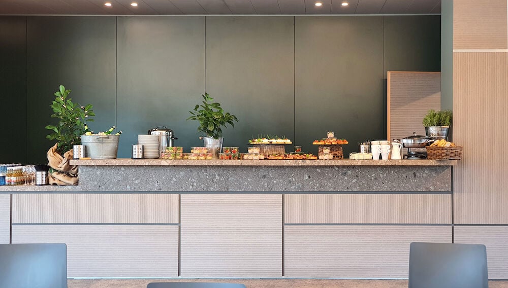 Moderne Buffettheke mit Frontverkleidung aus vertikal strukturierten Faserzementtafeln in warmem Beigeton – kombiniert mit einer Naturstein-Arbeitsplatte und einer dunkelgrünen Rückwand ergibt sich ein harmonisches, hochwertiges Gestaltungskonzept für den Innenausbau mit architektonischem Anspruch.