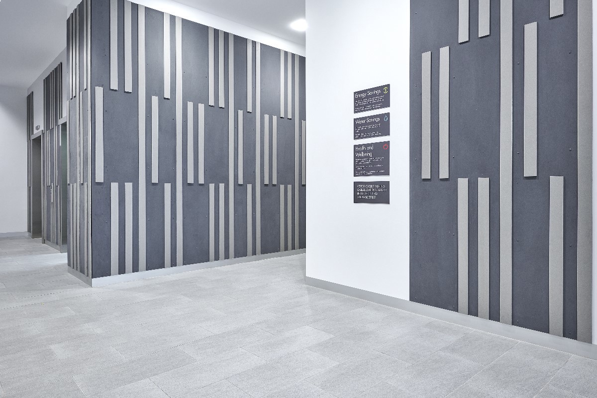 Innenraum mit wandintegriertem Design aus dunkelgrauen und hellgrauen Faserzementtafeln von EQUITONE – die vertikal angeordneten, unterschiedlich breiten Tafeln erzeugen ein dynamisches, modernes Muster und demonstrieren die gestalterische Vielfalt von Faserzement im Innenausbau.