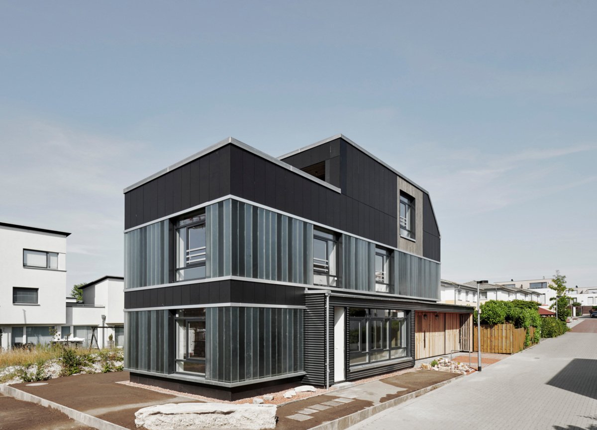 Modernes Wohngebäude mit dunkler Fassade aus EQUITONE Faserzementtafeln in Kombination mit transluzenten Elementen – die klare Linienführung und der Materialmix unterstreichen die architektonische Präzision und schaffen ein spannungsvolles Spiel aus Licht, Struktur und Transparenz.