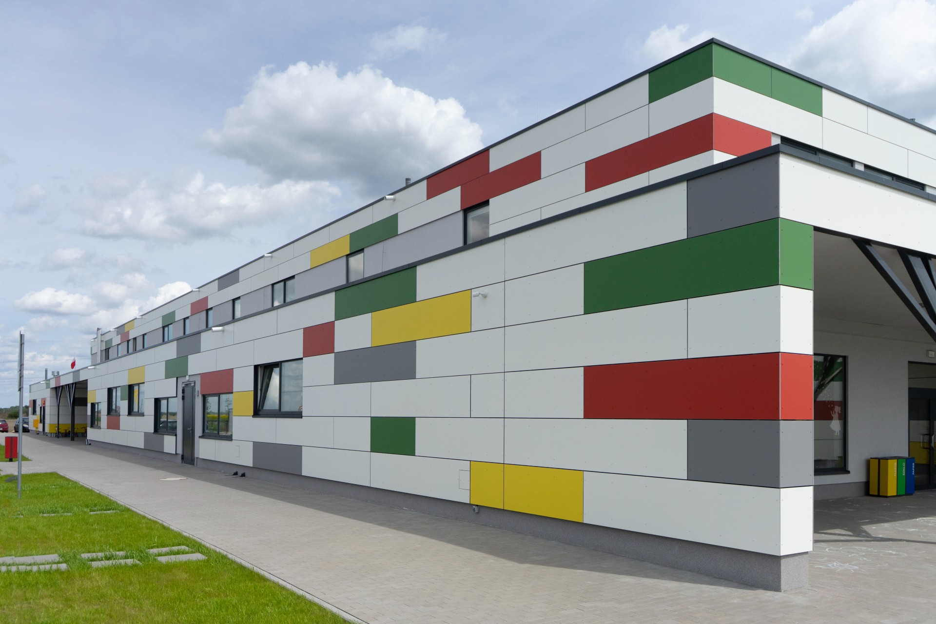 Kindergarten building featuring EQUITONE [coloura] fibre cement panels in red, green, yellow, white, and grey. The ventilated façade uses a playful colour scheme with modular cladding layout for a vibrant, low-maintenance educational facility.
