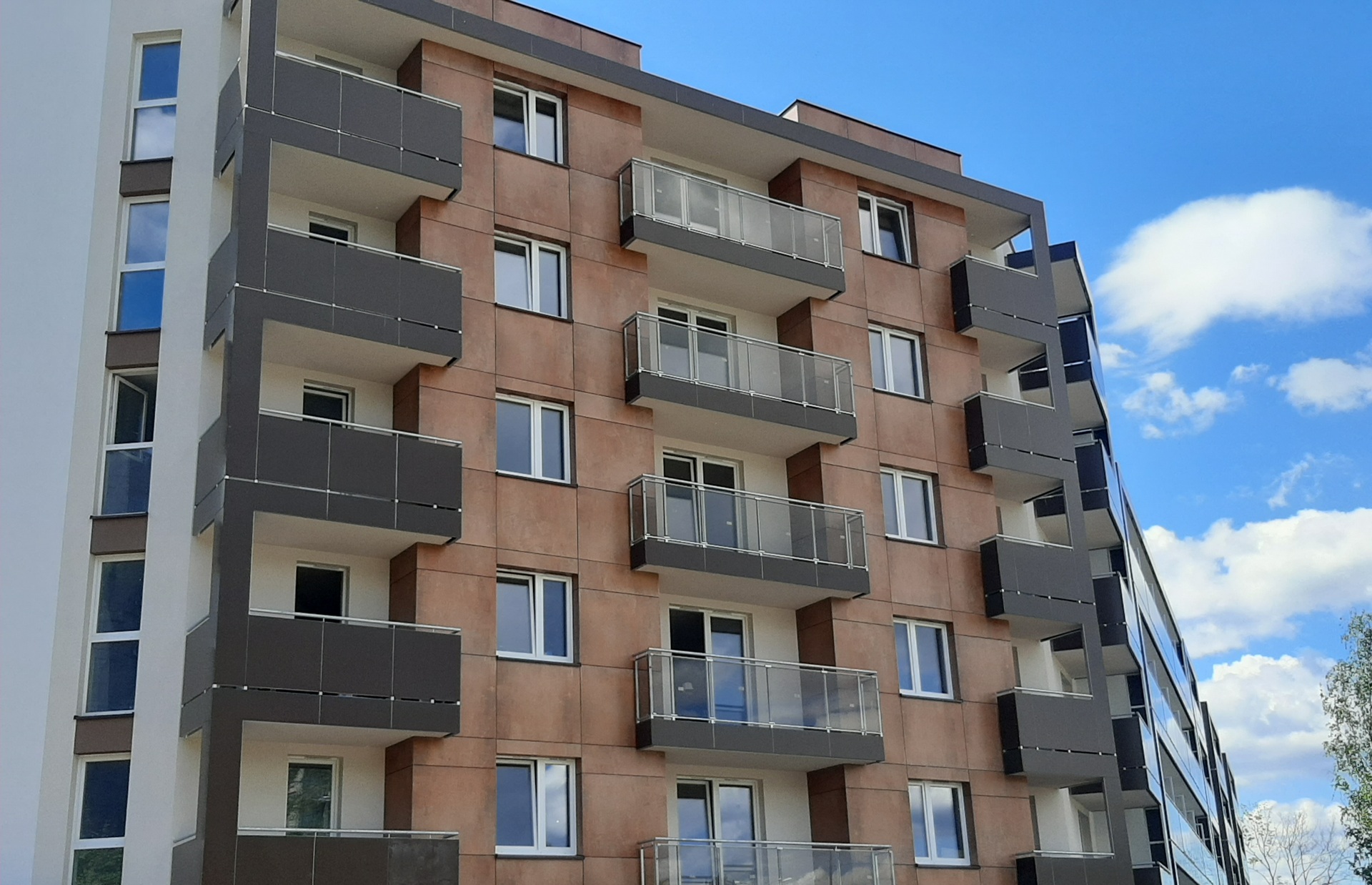 Modern mid-rise apartment facade clad with EQUITONE [inspira] fibre cement panels in rust-tone finish, featuring clean balconies and vertical lines